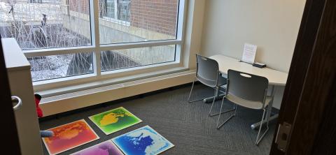 Room with white walls, gray floor, table with two chairs and sensory mats on the floor