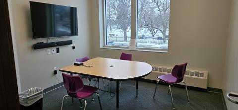 Table with four chairs and a tv; window in the background