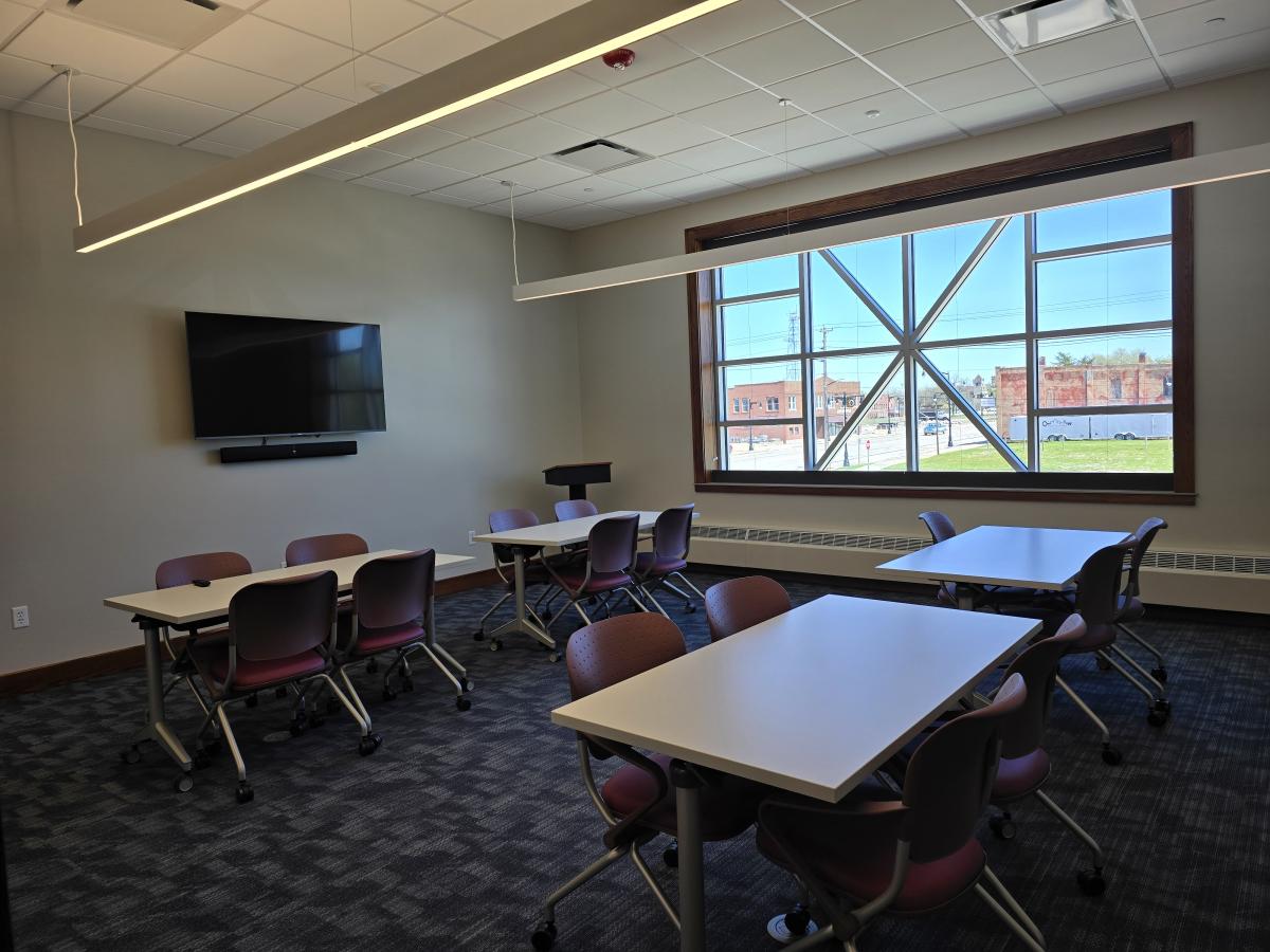 room with four tables and chairs, a tv, and a window in the background